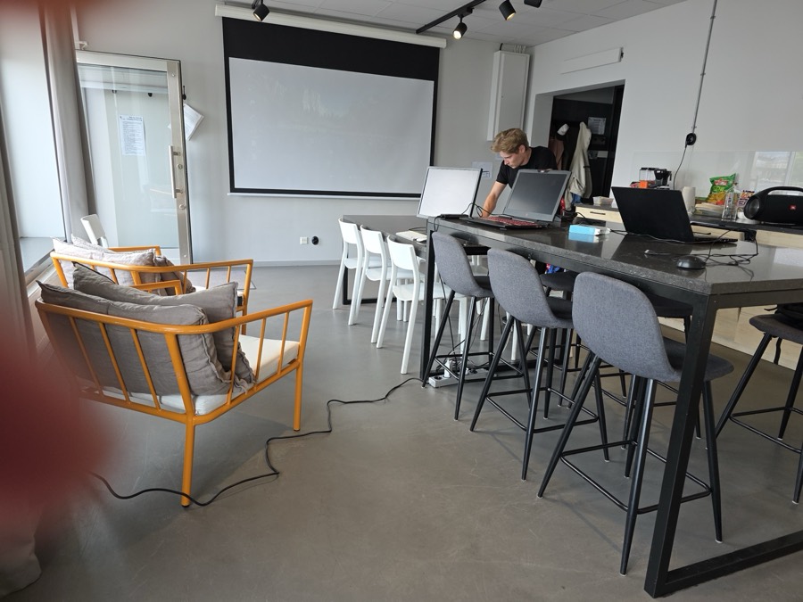 Bright workspace being set up with laptops on a high table and a projector screen