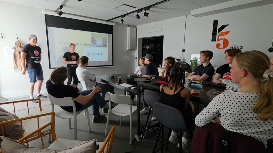 Wide view of a workshop room with presenters and young participants around a long table